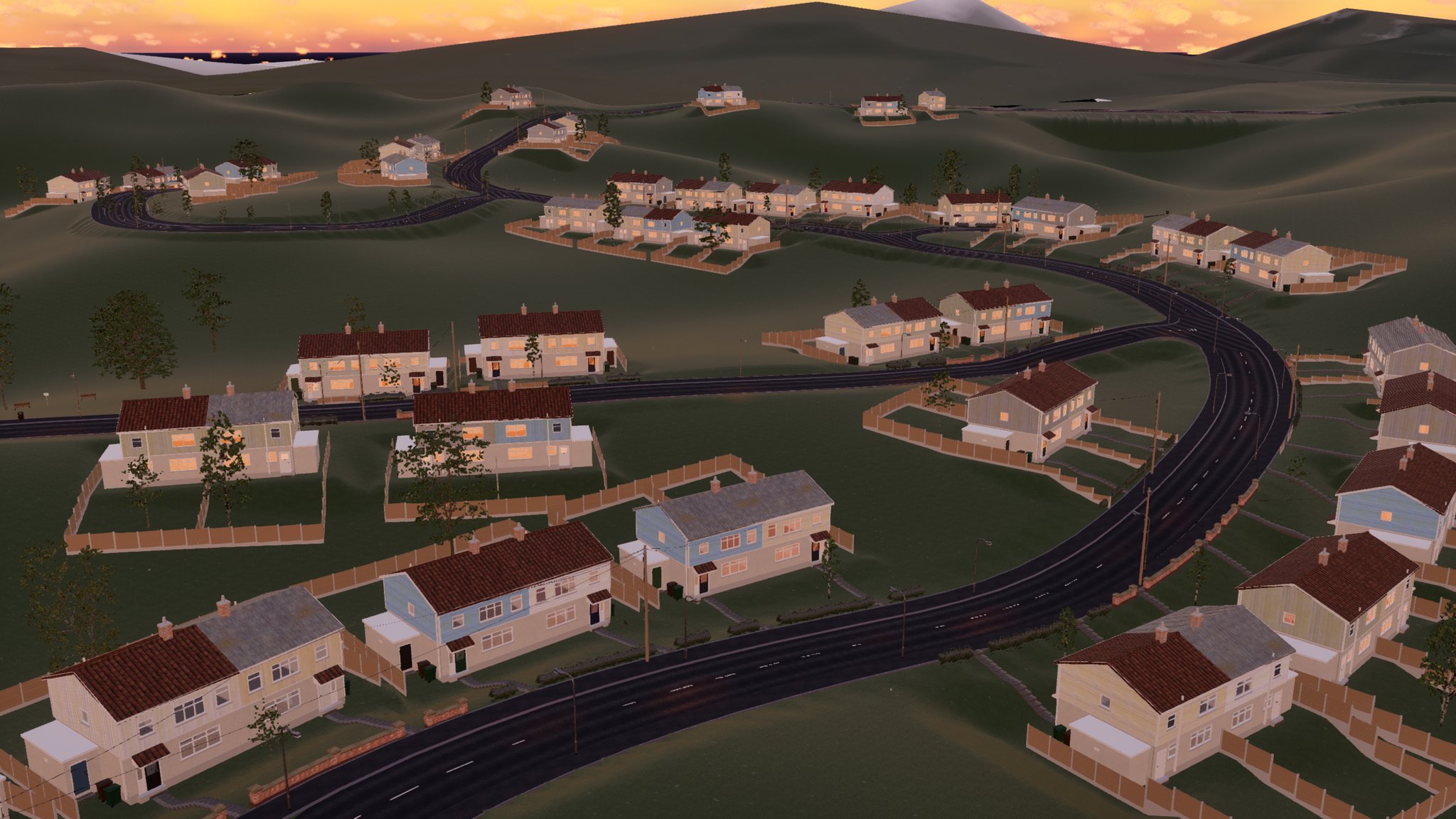 An aerial view of a new estate in a valley in golden evening light. Pairs of houses with red and grey roofs sit on levelled plots along a winding road, each with fenced back gardens, and a few trees stand on the greens between them. Grassy hills rise behind.