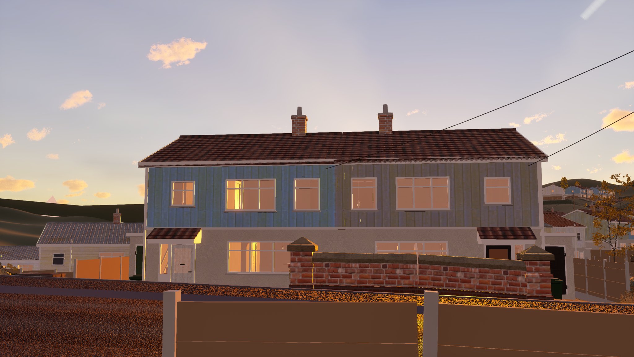 A pair of semi-detached houses in low evening sun. The ground floor is pale render; the upper storey is clad in vertical slats, blue on the left house and grey on the right, under a shallow tiled roof with two chimney stacks. A low brick garden wall with piers runs along the front, and an overhead wire runs from the roof to a pole out of frame.