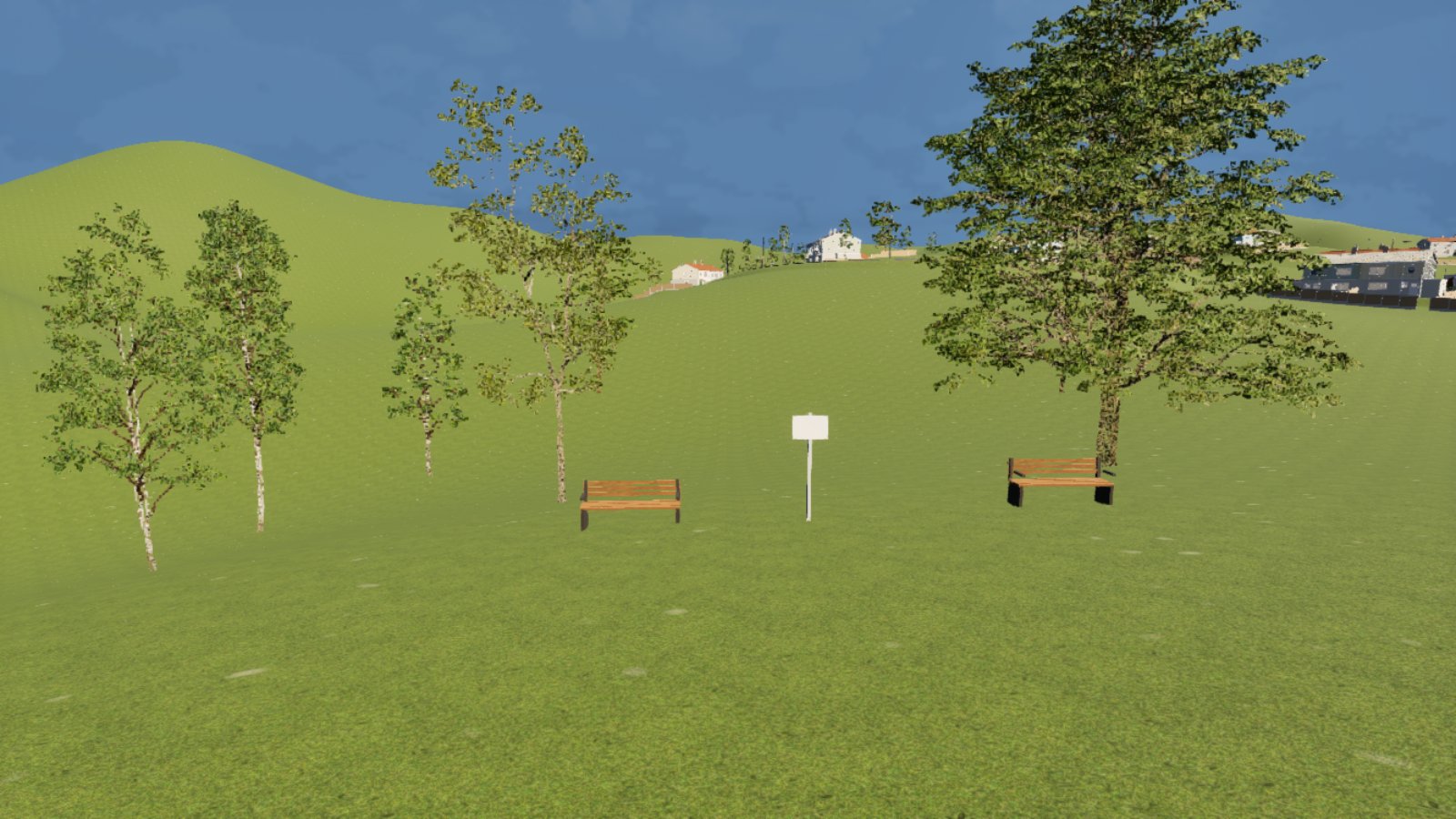 A grassy green on a hillside under a blue sky. Two wooden benches and a small blank white sign on a post stand in the middle, with thin young birch trees on the left and one larger tree on the right. Pale houses sit along the hill in the distance.