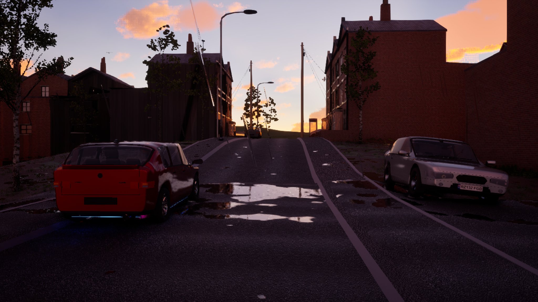 Sunset over a terraced street climbing a hill. A red hatchback drives away from the camera past a puddle on the tarmac; a silver car is parked on the right.