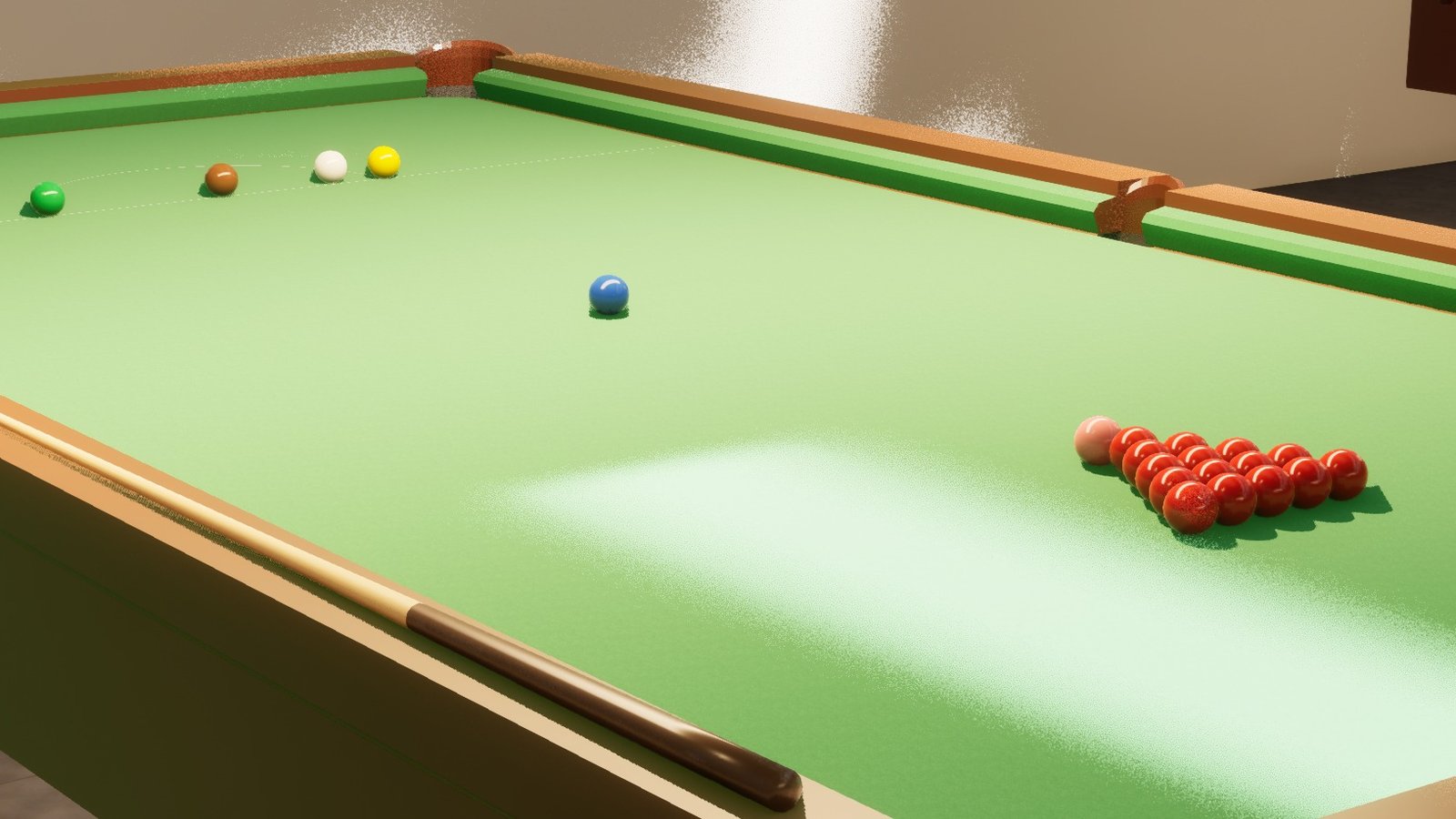 A close view along the bed of a snooker table. The baulk line and the curve of the D are marked in white on the green cloth, with the green, brown, white and yellow balls sitting on their spots along it, the blue on the centre spot, and the racked reds and the black away to the right. A cue rests on the near cushion, and the weave of the cloth is visible across the whole bed.