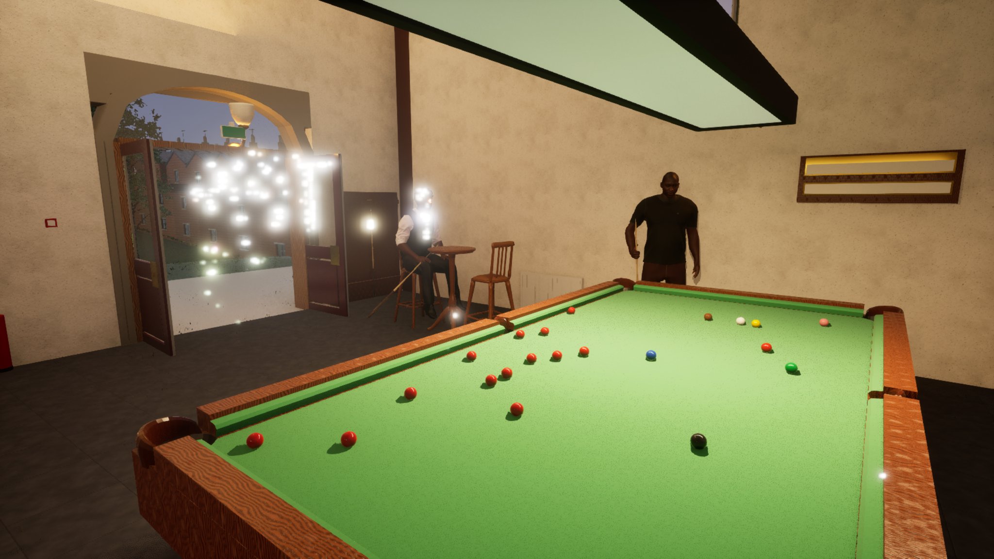 A full-size snooker table seen from the baulk end, mid-frame: the reds are scattered across the far half, with the black near the right cushion and the colours spread along the top. The bearded man in the black t-shirt stands at the far end; the man in the waistcoat sits at a small round table by the open doors, where strings of fairy lights outside bloom into a bright white haze. A long rectangular lamp hangs over the table at the top of the frame.