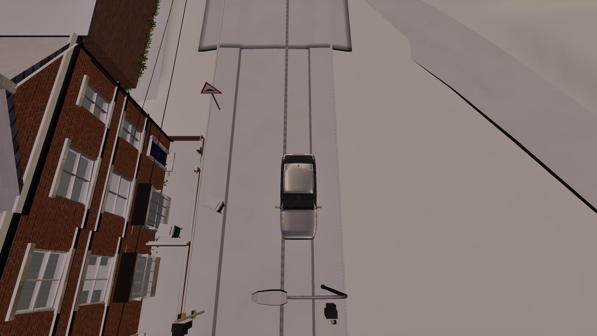 Looking straight down on a snow-covered road beside a red-brick terrace. A silver hatchback drives up the middle and behind it run two grey tyre tracks at its wheel spacing, alongside older tracks further over.