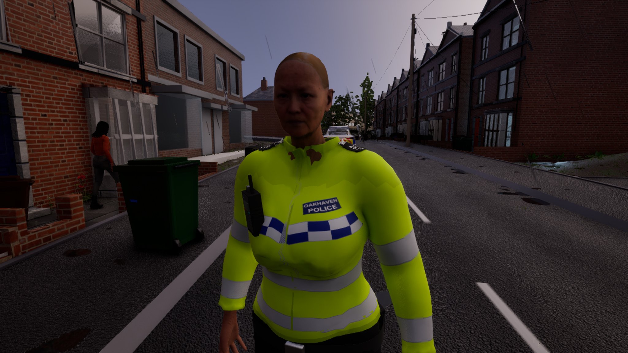 A police officer in a yellow hi-vis jacket marked Oakhaven Police stands close in front of the camera on a terraced street at dusk, the patrol car behind her and a woman walking away along the pavement.