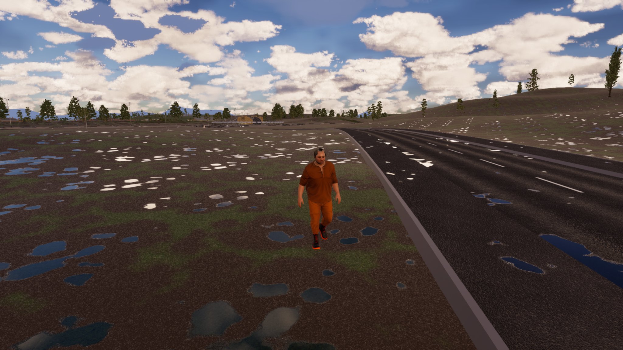 A man in an orange hi-vis top and trousers walks along the grass verge beside an empty two-lane road under a big cloudy sky, with low buildings on the horizon.