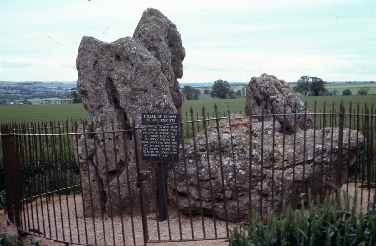 Several huge, weathered standing stones leaning together in a field, the remains of an ancient burial chamber.